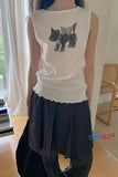Person wearing a white sleeveless top with cat designs and dark pants indoors.