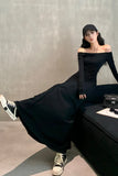 Woman in a black off-shoulder dress sitting on a couch with a gray wall background