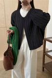 Person wearing a black textured jacket, white pants, and holding a brown bag.