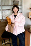 Person wearing a pink checkered jacket holding a loaf of bread indoors.