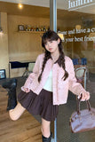 Woman in a pink jacket and black skirt holding a brown handbag in an indoor setting.
