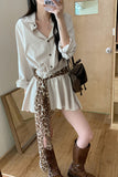 Person wearing a white shirt, leopard print skirt, and brown boots in a room.