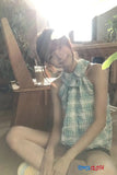 Person wearing a checkered dress sitting outdoors with plants in the background