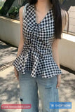 Person wearing a black and white checkered top with blue jeans outdoors.