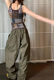 Person wearing a plaid tank top and green pants against a neutral background