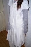 Person wearing a white outfit with a long coat and skirt in a room.