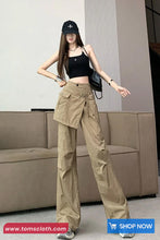 Woman wearing beige cargo pants and black top in a modern interior setting with 'tomscloth.com' branding.