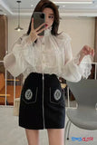Woman taking a mirror selfie wearing a white lace blouse and black skirt with embroidery.