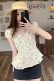 Woman taking a mirror selfie wearing a floral blouse and straw hat indoors.