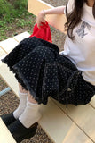 Person wearing black polka dot pants and a white shirt with a graphic design, sitting on a wooden bench.