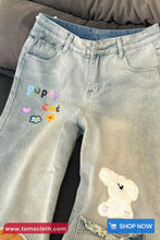 Light blue jeans with colorful text and a cartoon character, displayed on a gray surface.