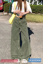 Person wearing green wide-leg pants and a white shirt, standing on a street.
