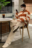 Person wearing a striped sweater and beige pants sitting at a table indoors.
