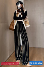 Person wearing a stylish outfit with a coat, pants, and bag in a room.
