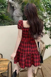 Woman wearing a red plaid dress sitting outdoors with plants and a statue in the background.