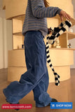 Person wearing blue pants and a striped shirt with a zebra-striped cat toy, standing in a room with wooden furniture.