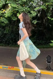 Woman walking outdoors with a patterned skirt and white bag, surrounded by greenery.