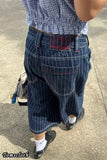 Person wearing a blue checkered shirt and dark blue pinstripe pants with a brand logo on a concrete surface.