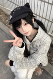 Person wearing a black cap and checkered shirt, making a peace sign outdoors.