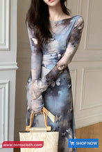 Woman wearing a long, sheer dress with butterfly design holding a beige handbag.