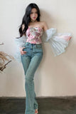 Woman wearing a floral top and jeans against a plain wall.