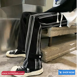 Person wearing black pants with white stripes and white sneakers on a concrete floor.