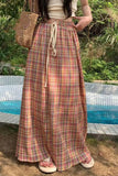 Person wearing a long plaid skirt by a poolside with greenery in the background