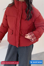 Person wearing a red puffer jacket with a plaid lining, standing against a white background.