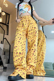 Person wearing a white crop top with colorful designs and yellow pants with brown spots in an indoor setting.