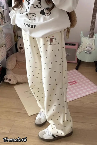 Person wearing a white hoodie with cartoon designs and polka dot pants in a room.