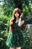 Woman in a green dress standing in a garden with trees and plants around.