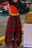 Person wearing a black top and red plaid pants with a brown backpack on a street.