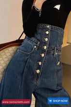 Person wearing a black top and blue jeans with button details, sitting on a chair.