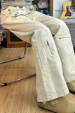 Person wearing beige cargo pants sitting on a chair with a guitar and other items in the background.