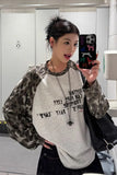 Person wearing a leopard print and gray sweater with text, holding a phone with a colorful case.