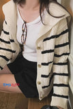 Person wearing a cream cardigan with black stripes and a white shirt, sitting indoors.