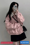 Person wearing a pink jacket and black skirt with a gray background, taking a mirror selfie.