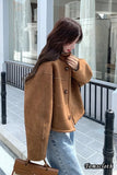 Person wearing a brown jacket and blue jeans standing on a sidewalk.