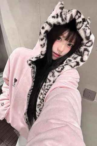 Person wearing a pink hoodie with a leopard print hood in an indoor setting