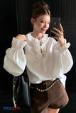 Woman taking a mirror selfie wearing a white blouse with puffed sleeves and brown shorts.