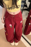 Person wearing a yellow crop top with text and red pants with floral designs, standing indoors.