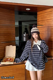 Woman in a striped sweater and white skirt standing in a kitchen with a pizza box.