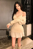 Woman in a beige sweater and skirt standing indoors.