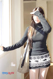 Woman wearing a black turtleneck and patterned skirt, holding a beige bag indoors.