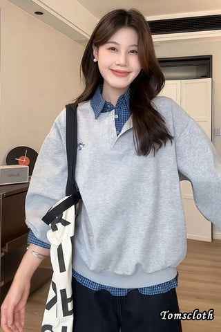 Woman wearing a gray sweater over a checkered shirt with a black and white bag, indoors.