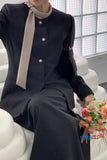 Person wearing a black outfit with a beige scarf, sitting on a white chair holding flowers.