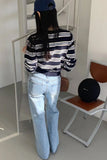 Person wearing a striped shirt and jeans standing in a room with a chair and black spherical object.