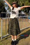 Person wearing a white t-shirt with a graphic design and camouflage pants, standing outdoors.