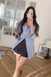 Woman taking a mirror selfie wearing a blue striped shirt and black skirt in a room with wooden flooring.