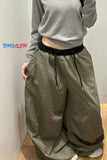 Person wearing olive green wide-leg pants with a gray top against a plain wall.